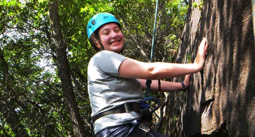 a student pauses to smile at the camera while rock climbing on an outdoor leadership course for lgbtq teens